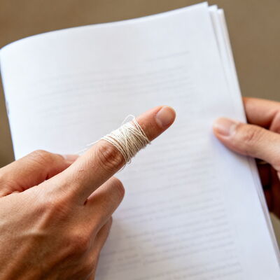 KI generiertes Bild. Hand mit umwickeltem Zeigefinger zeigt auf eine Seite eines gedruckten Dokuments.